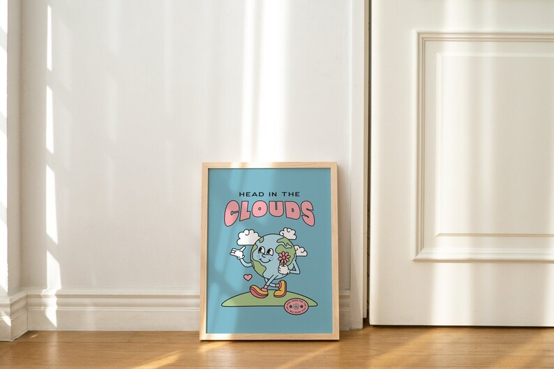May include: A framed print with a blue background and a cartoon illustration of the Earth holding a flower. The text "HEAD IN THE CLOUDS" is written in pink letters above the Earth.
