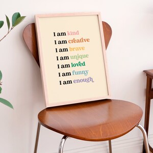 Op de afbeelding: Een ingelijst print met een cr&egrave;mekleurige achtergrond en zwarte tekst die luidt: "Ik ben aardig, ik ben creatief, ik ben dapper, ik ben uniek, ik ben geliefd, ik ben grappig, ik ben genoeg."