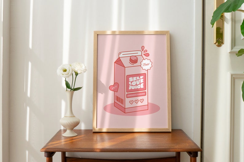 May include: A framed print with a pink background featuring a cartoon illustration of a pink carton of "Self Love Juice" with a red heart and the text "Fresh!" in a white circle. The carton has a barcode and three red hearts on the front.