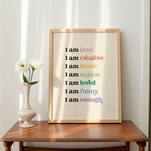 Op de afbeelding: Een ingelijst print met een witte achtergrond en de tekst "Ik ben aardig", "Ik ben creatief", "Ik ben dapper", "Ik ben uniek", "Ik ben geliefd", "Ik ben grappig" en "Ik ben genoeg" in verschillende kleuren.