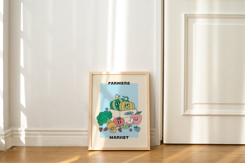May include: A framed print with a light blue background featuring a cartoon illustration of a box of produce with the text "FARMERS MARKET". The box contains a green and yellow pumpkin, a red apple, a green pea pod, a yellow lemon, and a green broccoli.