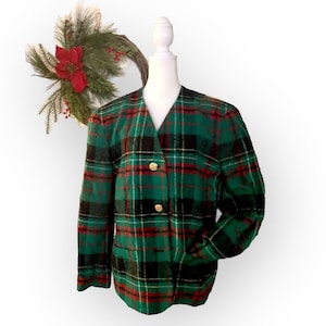 May include: A green, red, black, and white plaid blazer with gold buttons. The jacket has a V-neck and two pockets. The blazer is displayed on a mannequin. A wreath with a red flower is in the background.
