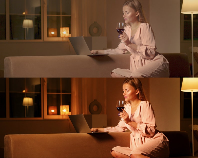 May include: A woman sits on a couch in a dimly lit room, holding a glass of red wine and using a laptop. She is wearing a light pink dress.