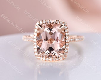 May include: A rose gold engagement ring with a cushion-cut morganite center stone surrounded by a halo of smaller diamonds. The band is also set with smaller diamonds.