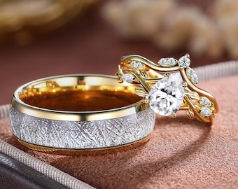 May include: Two wedding rings. One is gold with a textured silver band and a gold interior. The other is a gold band with a pear-shaped diamond and leaf accents. The rings are displayed in a brown ring box.