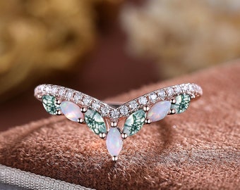 May include: A delicate, curved wedding band with a V-shaped design. The band is set with small, round diamonds and larger, oval-shaped opals and green gemstones.