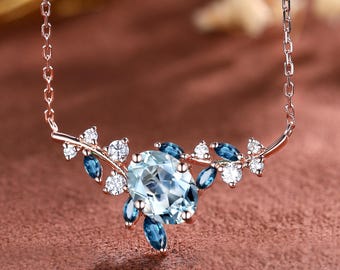 Puede incluir: Un collar de oro rosa con una piedra preciosa azul claro central, rodeada de piedras azules y blancas más pequeñas. El collar tiene un diseño floral delicado, con una cadena que se conecta al colgante.