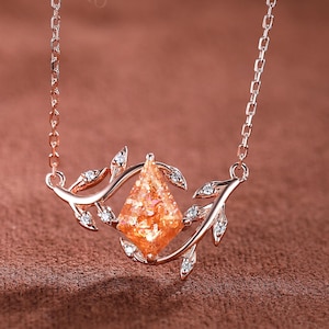 May include: A delicate rose gold necklace with a sunstone pendant set in a diamond-shaped frame. The pendant is surrounded by two intertwining branches with small leaves and diamonds.