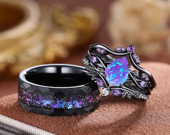 Puede incluir: Dos anillos negros. Uno tiene una banda con un diseño de galaxia en morado y azul. El otro anillo tiene una banda negra con una piedra central de ópalo azul-púrpura en forma de lágrima, rodeada de detalles morados y un diseño floral.
