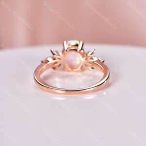 May include: A rose gold ring with a white opal center stone and smaller accent stones. The ring is set in a delicate, floral design.