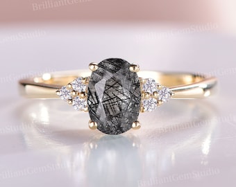 May include: A gold engagement ring with a black and gray oval-shaped gemstone surrounded by smaller clear gemstones.