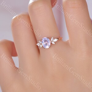 May include: A rose gold engagement ring with a light purple oval-shaped gemstone surrounded by smaller clear gemstones. The ring features a delicate leaf design.