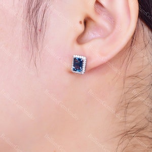 May include: A pair of silver stud earrings with a blue gemstone surrounded by smaller white gemstones.