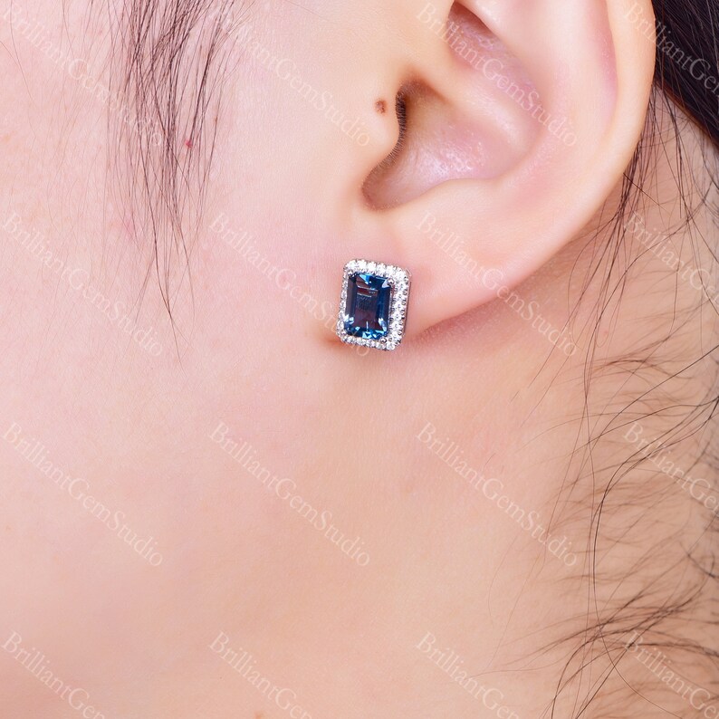 May include: A pair of silver stud earrings with a blue gemstone surrounded by smaller white gemstones.