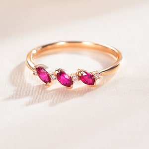 May include: A delicate gold ring with three marquise-shaped ruby stones and small diamonds set in the band.