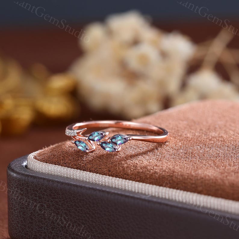 May include: A rose gold ring with a delicate branch design featuring five marquise-shaped blue gemstones. The ring is set on a brown velvet surface.