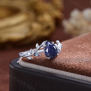 May include: A silver ring with a blue gemstone set in a leaf design. The ring is in a box with a brown velvet lining.