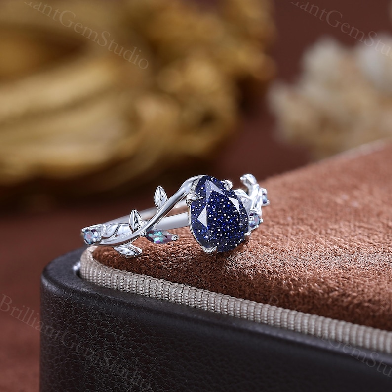 May include: A silver ring with a blue gemstone set in a leaf design. The ring is in a box with a brown velvet lining.