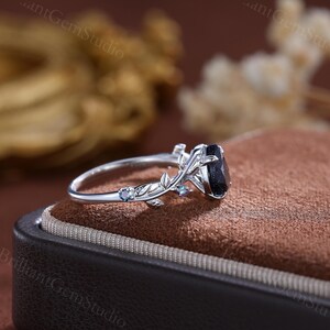 May include: A silver ring with a black oval gemstone set in a delicate floral design. The ring features two smaller blue gemstones on the band.