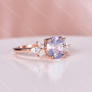 May include: A rose gold engagement ring with a large oval-shaped lavender gemstone surrounded by smaller clear gemstones. The ring has a delicate floral design.