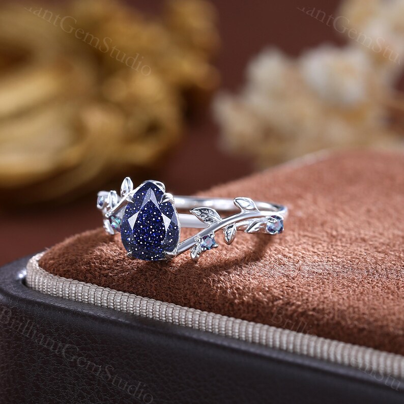 May include: A pear-shaped blue gemstone ring with a leafy design. The ring is set in silver and features a blue gemstone with a sparkly finish.