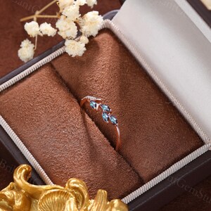 May include: A delicate rose gold ring with three marquise-shaped blue gemstones set in a vine-like design. The ring is displayed in a brown velvet ring box.