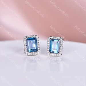May include: A pair of silver earrings with a square blue topaz gemstone surrounded by a halo of smaller diamonds.