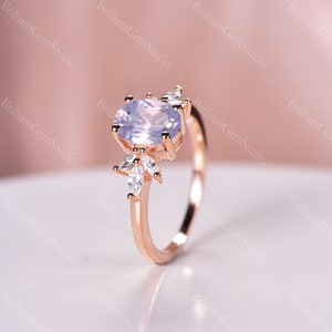 May include: A rose gold engagement ring with a light purple oval-shaped gemstone and smaller clear gemstones on the band.