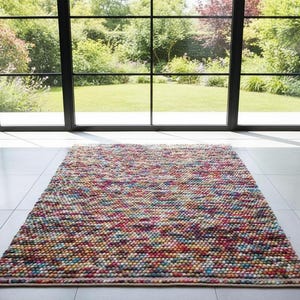 May include: A rectangular area rug with a colorful, textured surface. The rug is made of small, tightly packed, multi-colored balls in shades of pink, blue, yellow, and green. The rug is placed on a light-colored tile floor.