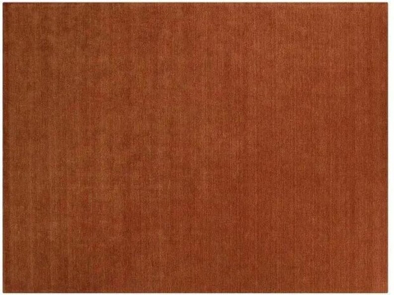 May include: A rectangular, solid rust-colored rug. The rug has a woven texture, with visible vertical lines. The color is a warm, earthy tone, suitable for various interior design styles. The rug is a large size.
