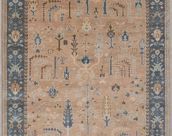 Pode incluir: Um tapete retangular com um campo bege e uma borda azul escuro. O tapete apresenta um padrão repetido de árvores estilizadas e motivos florais em tons de azul, castanho e bege. O tapete tem franjas nas bordas.