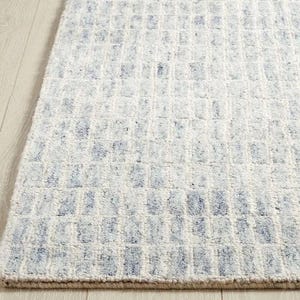 May include: A rectangular rug with a textured surface. The rug features a grid pattern in shades of white and light blue. The rug's edges are finished with a neutral-coloured border.