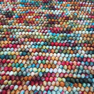 May include: A colorful rug composed of tightly packed, small, round felt balls. The rug features a vibrant array of colors, including red, orange, yellow, green, blue, and purple, creating a textured and visually appealing surface.