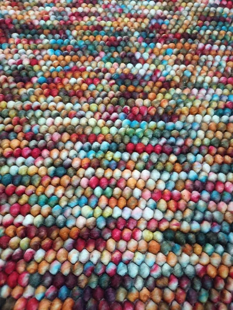 May include: A colorful rug composed of tightly packed, small, round felt balls. The rug features a vibrant array of colors, including red, orange, yellow, green, blue, and purple, creating a textured and visually appealing surface.