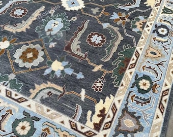May include: A rectangular, dark gray rug with an intricate floral and geometric pattern. The rug features a border in light blue, beige, and brown tones. The central design includes floral motifs in white, blue, and brown.