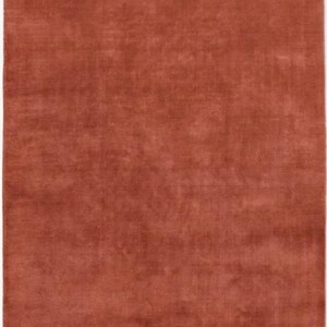 May include: A rectangular, solid rust-colored rug. The rug has a soft, plush texture and a uniform color throughout. The rug is a solid color and would be suitable for a living room or bedroom.