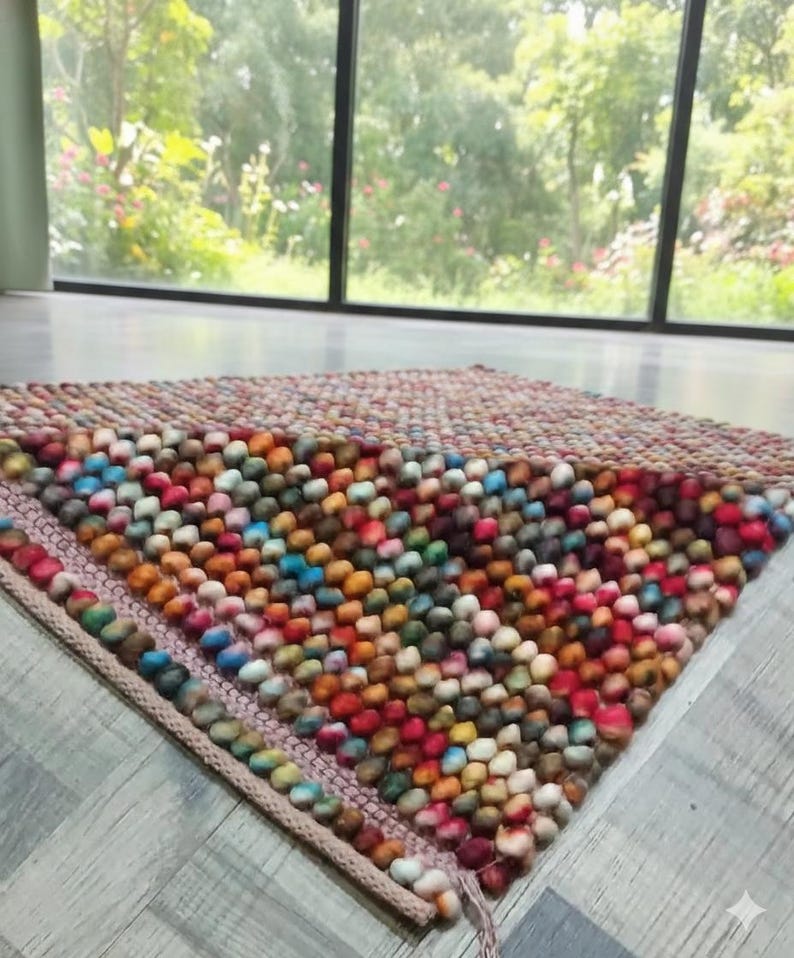 May include: A colorful, handmade rug with a textured surface. The rug is made of small, round, wool balls in a variety of colors, including red, orange, yellow, blue, and green. The rug has a rectangular shape and a woven border.