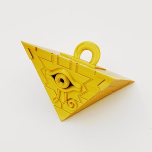 Peut inclure: Un pendentif triangulaire jaune vif en trois dimensions avec un symbole d'œil en relief au centre. L'objet présente une texture lisse et stratifiée, et comprend une petite boucle circulaire au sommet pour l'attache, rappelant une pyramide.