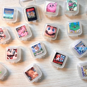 May include: A collection of clear plastic game cartridge cases, each containing a different game cartridge. The cases feature colorful graphics of characters and scenes from popular video games, including Mario, Pikachu, and Kirby.