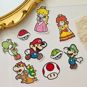 May include: A set of nine paper stickers featuring characters from the Super Mario Bros. video game franchise. The stickers are colorful and feature characters like Mario, Luigi, Princess Peach, Toad, and Bowser.