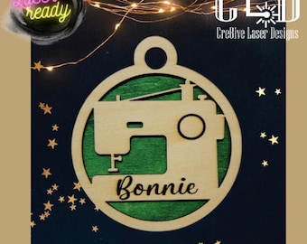 May include: A laser cut wooden ornament shaped like a sewing machine with the name "Bonnie" engraved on it. The ornament is green and brown and has a hole at the top for hanging.