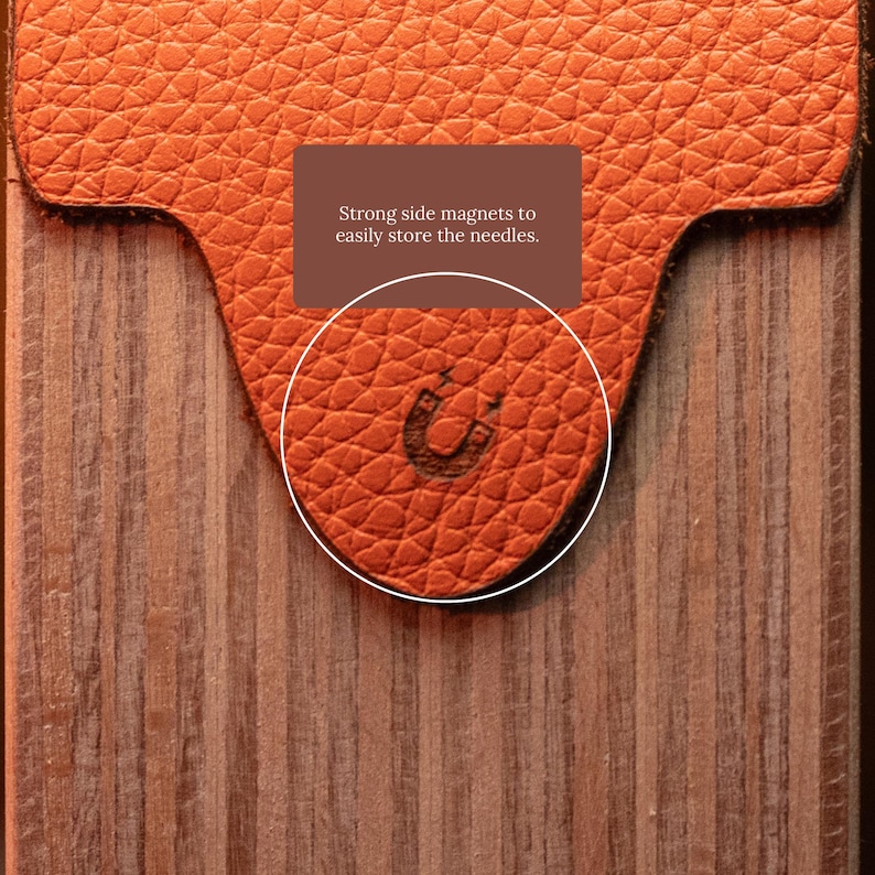 May include: A textured orange leather flap with a horseshoe magnet icon embossed on the surface, positioned over a vertical wood grain panel. The text on the flap reads: Strong side magnets to easily store the needles.