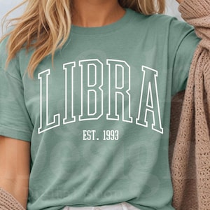 May include: A teal blue t-shirt with the word "LIBRA" in white outlined letters and the text "EST. 1993" underneath.