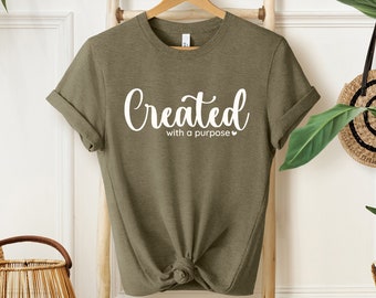 May include: A green t-shirt with the text "Created with a purpose" in white lettering. The shirt is knotted at the bottom and is hanging on a wooden ladder.