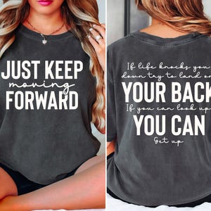 Puede incluir: Camiseta gris carbón con las frases "JUST KEEP moving FORWARD" en la parte delantera y "If life knocks you down try to land on YOUR BACK If you can look up YOU CAN Get up" en la trasera. La camiseta tiene un corte holgado.
