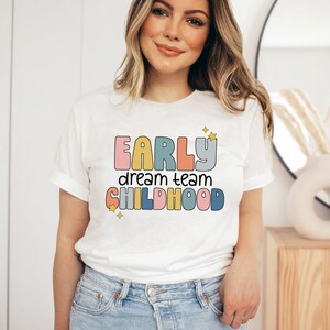 May include: White t-shirt with a colorful graphic that says "Early dream team childhood" with stars.