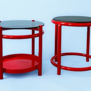 May include: Two red metal side tables with round tops. One table has a glass top and a lower shelf. The other table has a solid wood top.