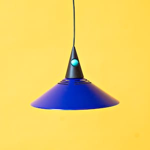 Può includere: Una lampada a sospensione blu con un cavo nero e un piccolo pulsante turchese in cima.