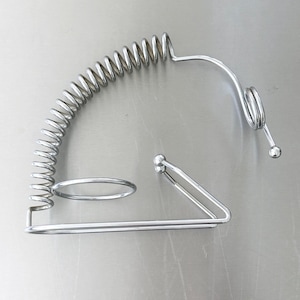 Op de afbeelding: Een zilverkleurige metalen standaard met een lange, gebogen spiraalveerstructuur bevestigd aan een driehoekige basis. Het ontwerp bevat een cirkelvormige ringbevestiging en een kleiner spiraalgedeelte aan de bovenkant met kleine bolvormige uiteinden.