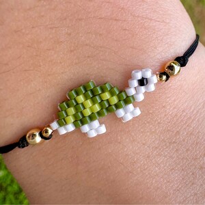 May include: A green and white beaded turtle charm bracelet with gold beads and a black cord.